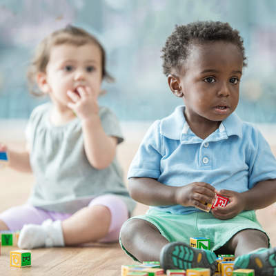 Babies play in a daycare together. They play with blocks. Here, a three babies play together.